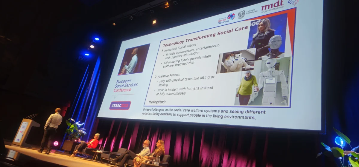Predavatelj na odru ESSC 2025 razlaga o uporabi humanoidnih in asistivnih robotov v socialnem varstvu, ob velikem zaslonu s predstavitvijo primerov uporabe robotike.