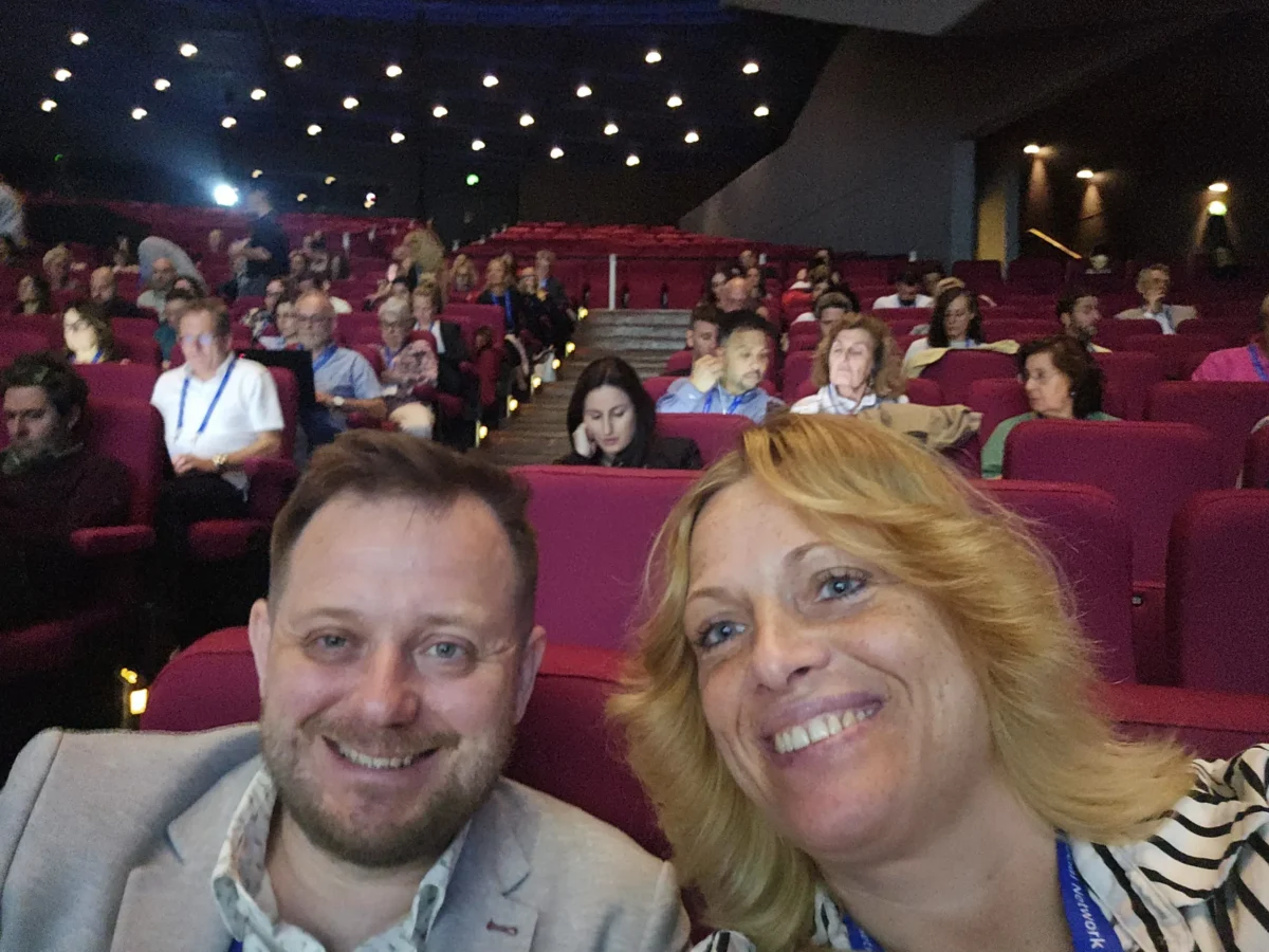 Nasmejana udeleženca konference ESSC 2025 med občinstvom, v ozadju dvorana s številnimi obiskovalci.