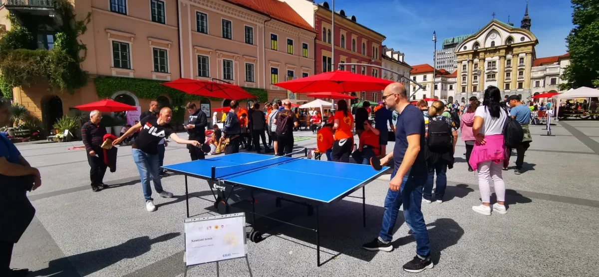 Dve osebi igrata namizni tenis na prostem med obiskovalci festivala.