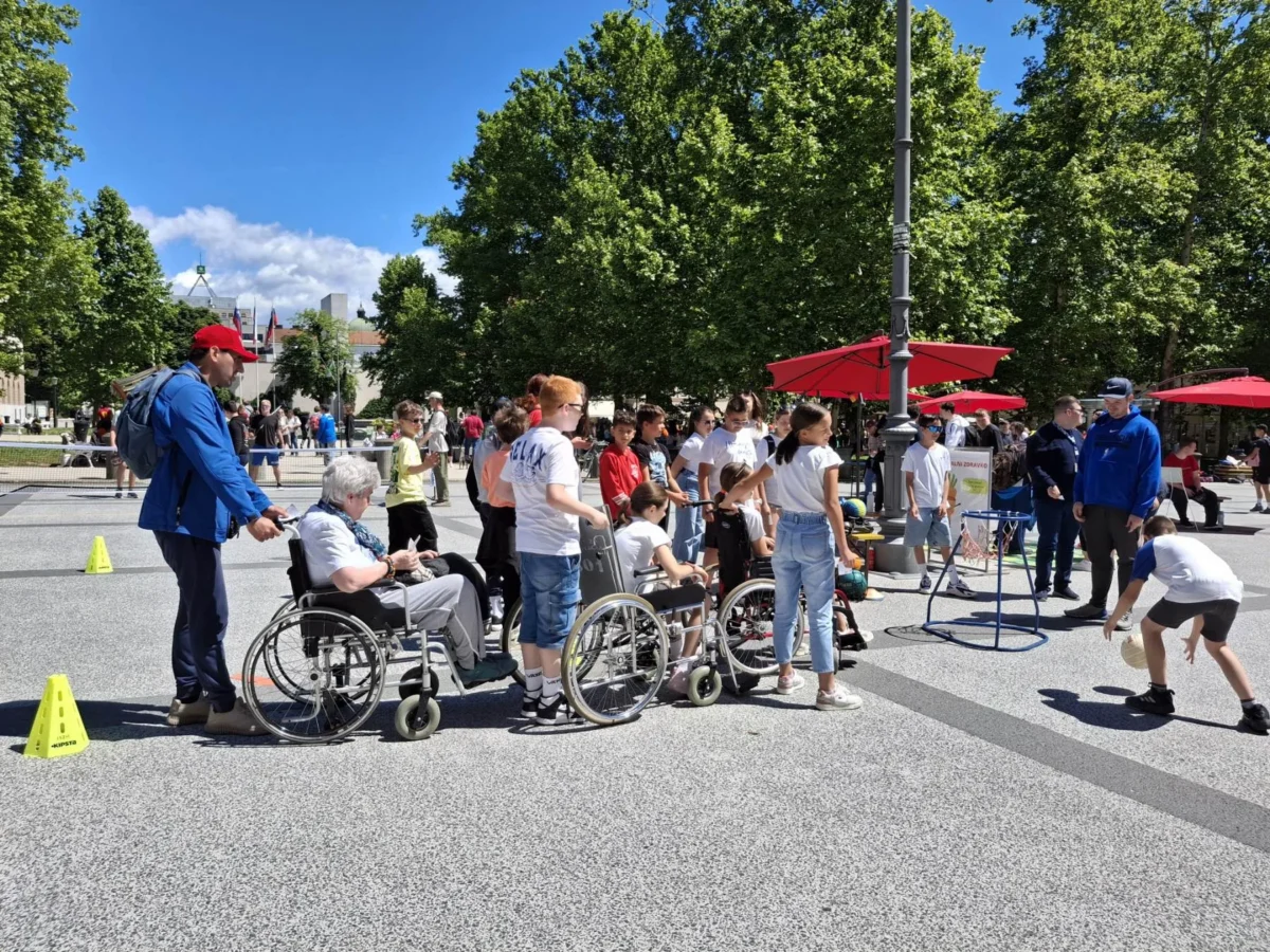 Udeleženci, med njimi tudi v invalidskih vozičkih, sodelujejo v športni igri na prostem.