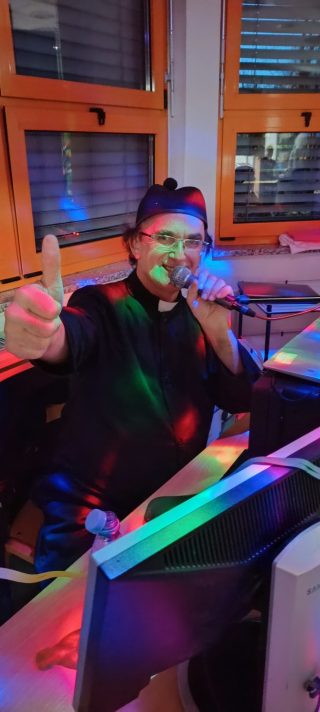 Posnetek pustnega rajanja v VDC Tončka Hočevar - glasbenik za klaviaturo, oblečen v duhovnika, v rokah drži mikrofon