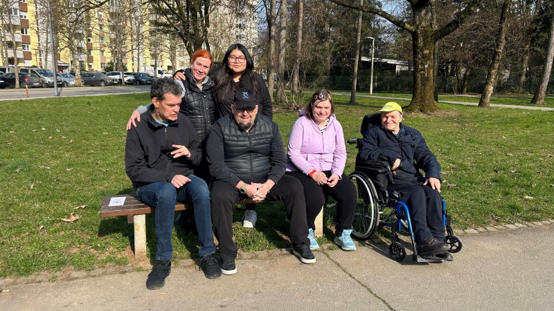 Varovanci VDC Tončke Hočevar in dijakinje iz Španije na sprehodu pozirajo na klopci
