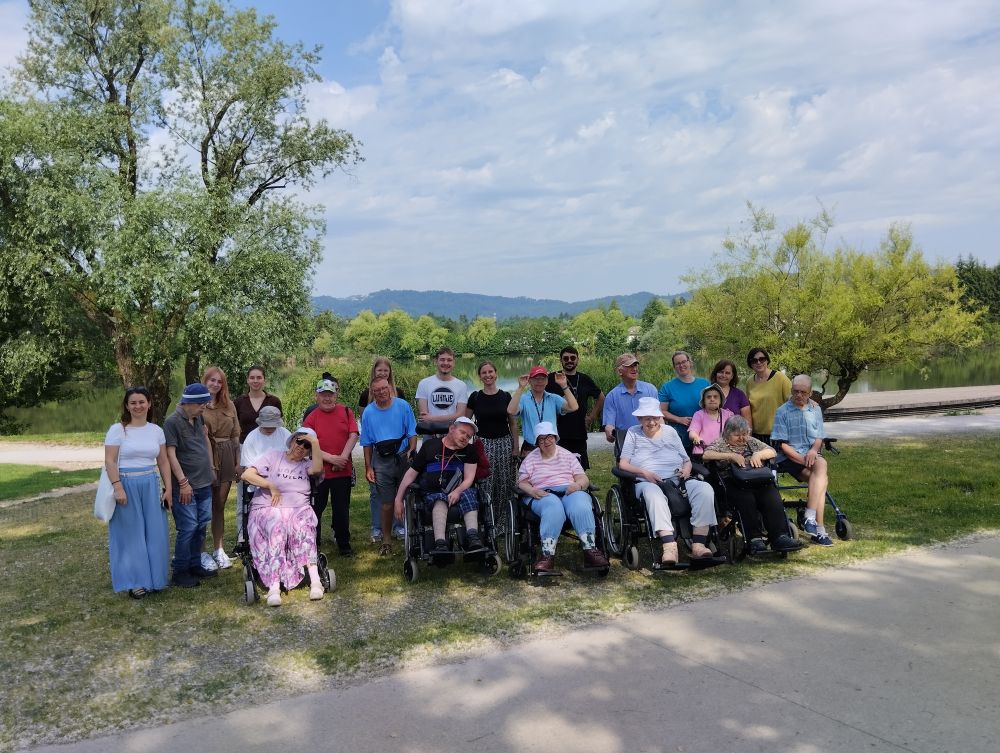 Skupina udeležencev stoji ob Koseškem bajerju na skupinski fotografiji, v ozadju so drevesa, voda in hribovje.