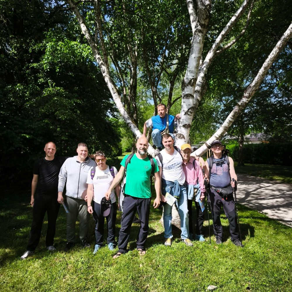 Skupina udeležencev stoji na travi ob drevesu med pohodom Pot ob žici in pozira za skupinsko fotografijo.