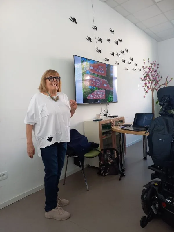 Prostovoljka vida stoji in na tv zaslonu predstvlja potopisno predavanje o Kubi
