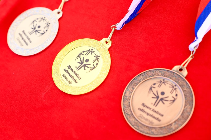 Zlata, srebrna in bronasta medalja na rdeči podlagi.