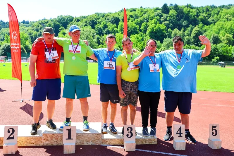 Tekmovalci z medaljami koli vratu, stojijo na odru za zmagovalce in se veselijo
