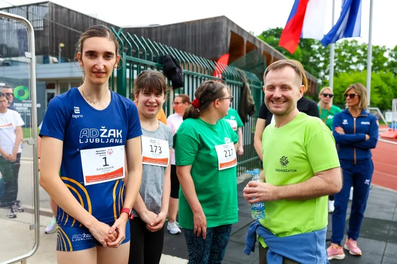Tri tekmovalke s štartnimi številkami na majicah in driektor Slavko Bolčevič pozirajo pred fotografom.