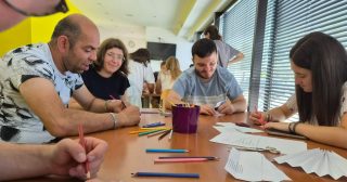 Uporabniki in prostovoljka iz Španije sodelujejo pri izdelavi origamija na ustvarjalni delavnici.