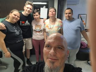 Spredaj ena oseba, ki fotografira sebe in osebe za njim, ki pozairajo, objeti čez ramena.