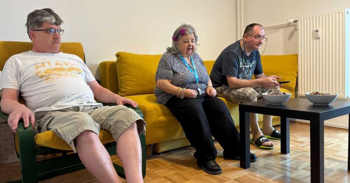 Uporabniki sedijo v dnevnem prostoru novega stanovanja na Celovški in skupaj preživljajo čas ob mizi.