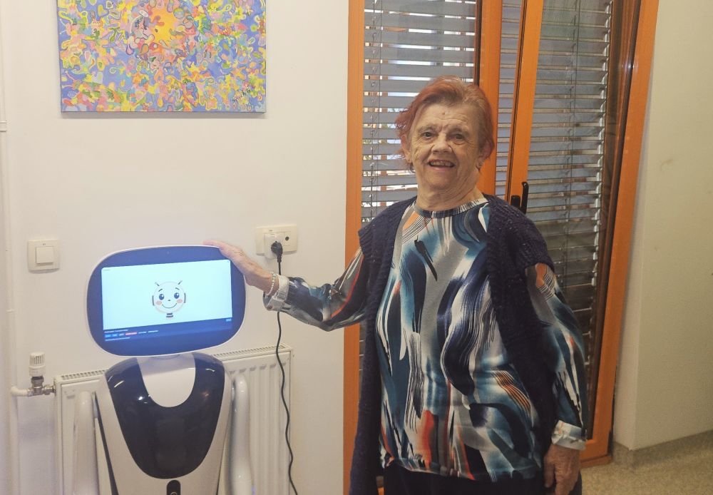 Uporabnica VDC Tončke Hočevar stoji ob socialnem robotu Timu, ki je namenjen podpori osebam z motnjo v duševnem razvoju.
