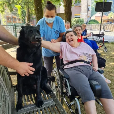 Varovanci in skrbniki uživajo ob družbi črnega psa, ki sedi kar na klopi.