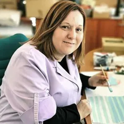 Varovanka pozira za mizo, na keteri je list, v rokah drži čopič in pozira ob risanju